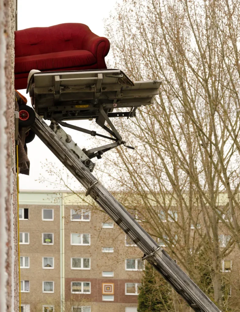 Möbelaufzug transportiert ein rotes Sofa an einer Hauswand nach oben