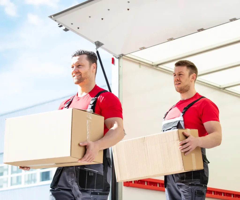 Zwei Umzugshelfer tragen Kartons aus einem Transporter